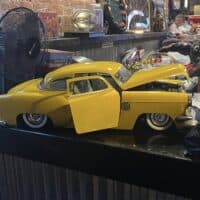 A detailed yellow classic car model with open hood, displayed on a table at Do it a-Ginn Event Hall, showcasing vintage decor and collectibles in the background.