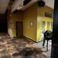 Dated photo of the interior at Do It A-Ginn Event Hall, showcasing a cozy event space with a yellow accent wall, decorative mirrors, and wooden flooring, perfect for hosting various celebrations and gatherings in a rustic setting.