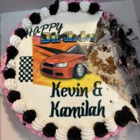 Delicious birthday cake with race car theme, decorated with black, white, and pink icing, perfect for a celebratory event at Do It a-Ginn Event Hall.